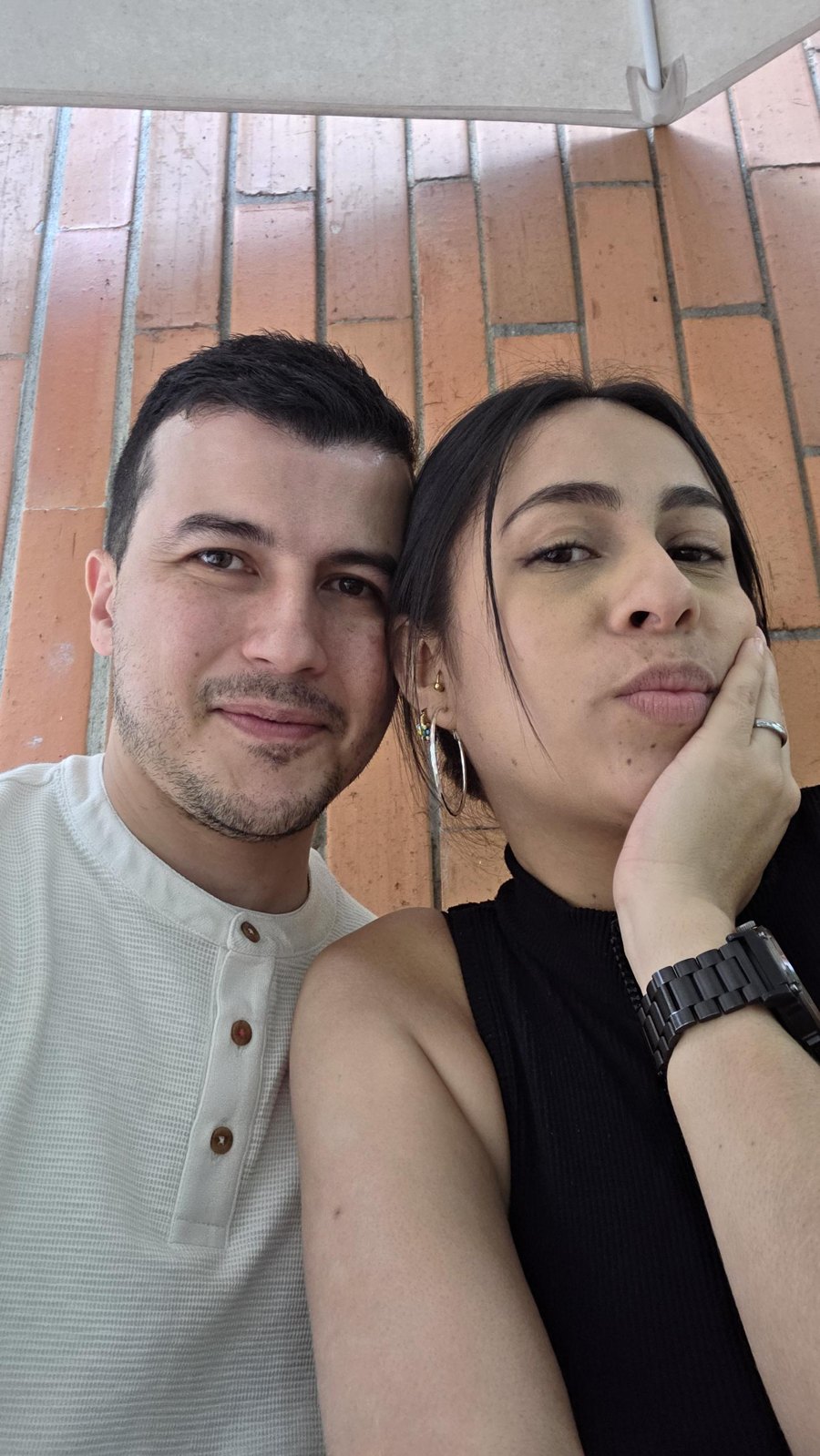 Selfie de Daniela y Anderson frente a una pared de ladrillo
